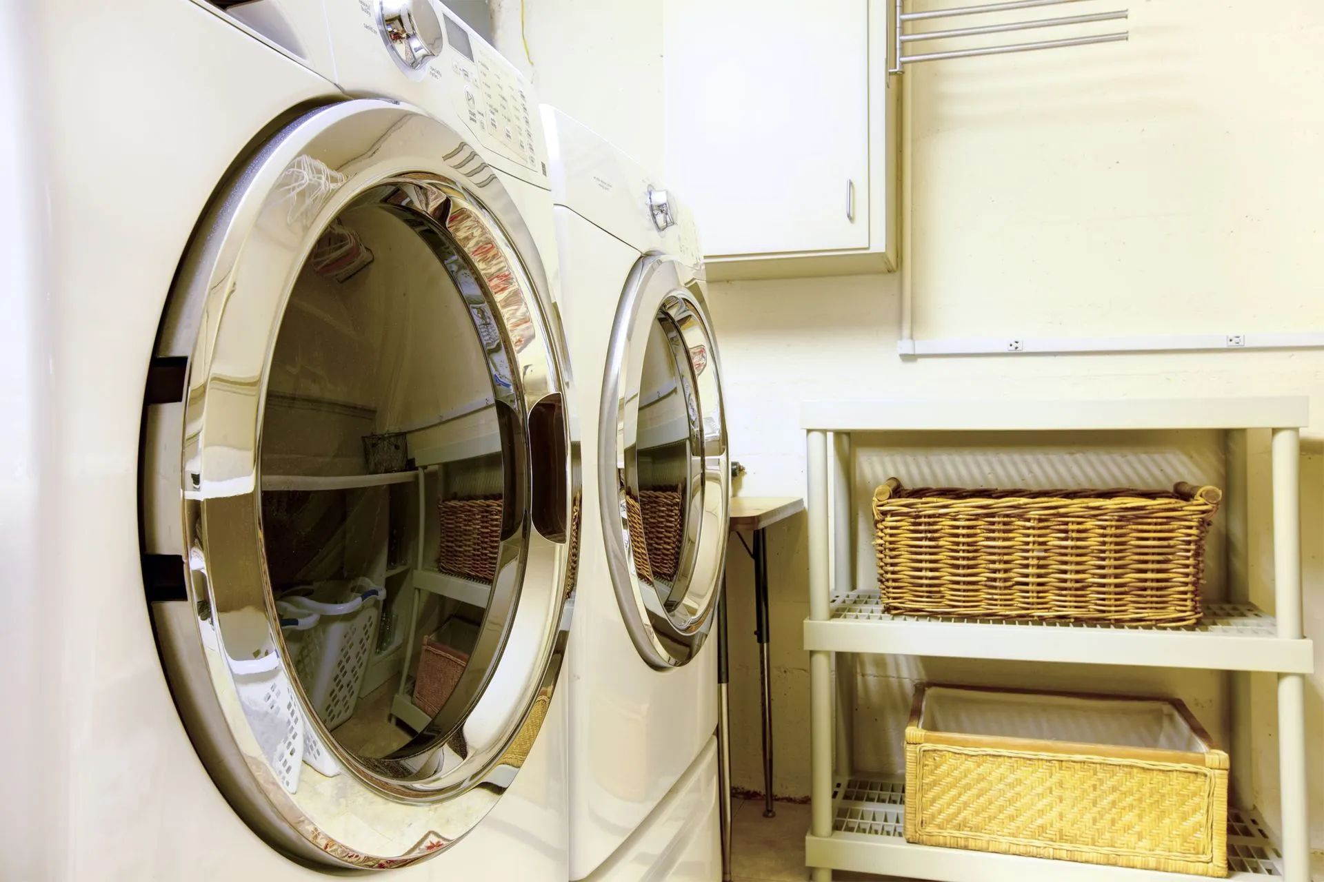 White washer and dryer in a laundry room; shelves with baskets sit beside them.