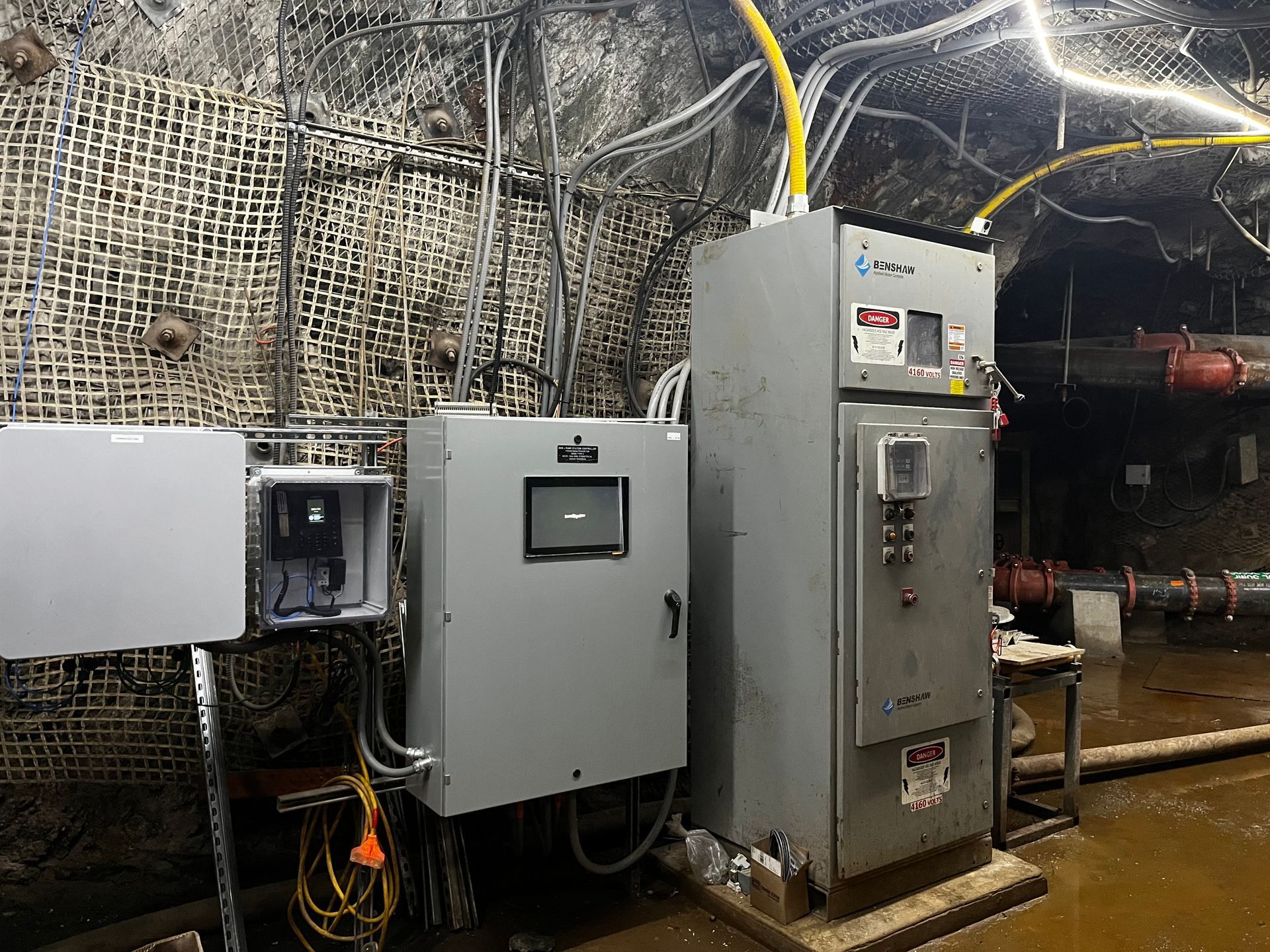 Electrical control panels inside a tunnel, with various wires and equipment mounted on a wall.