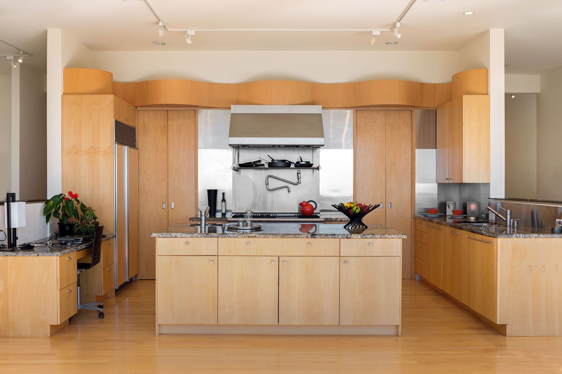 A modern kitchen featuring light-wood cabinetry, a central island, stainless steel appliances, and track lighting.