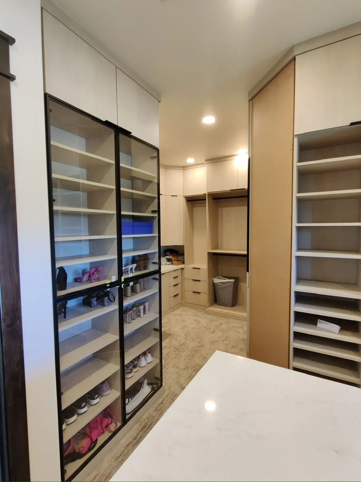 A modern walk-in closet featuring floor-to-ceiling glass-front cabinets, open shelving, and a central white island.