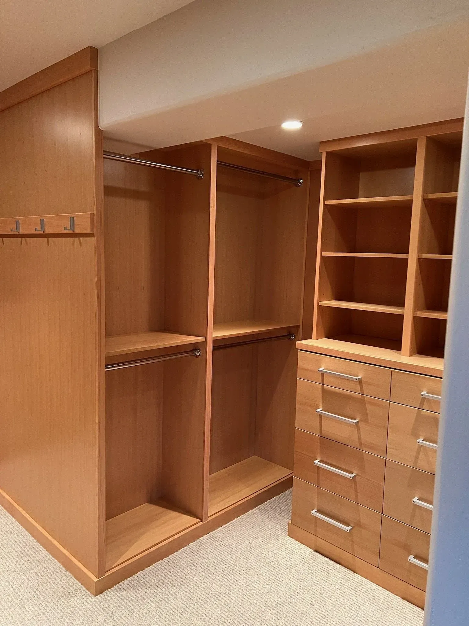 Light wood custom closet organizer featuring hanging rods, shelving, and a set of stacked drawers on a carpeted floor.