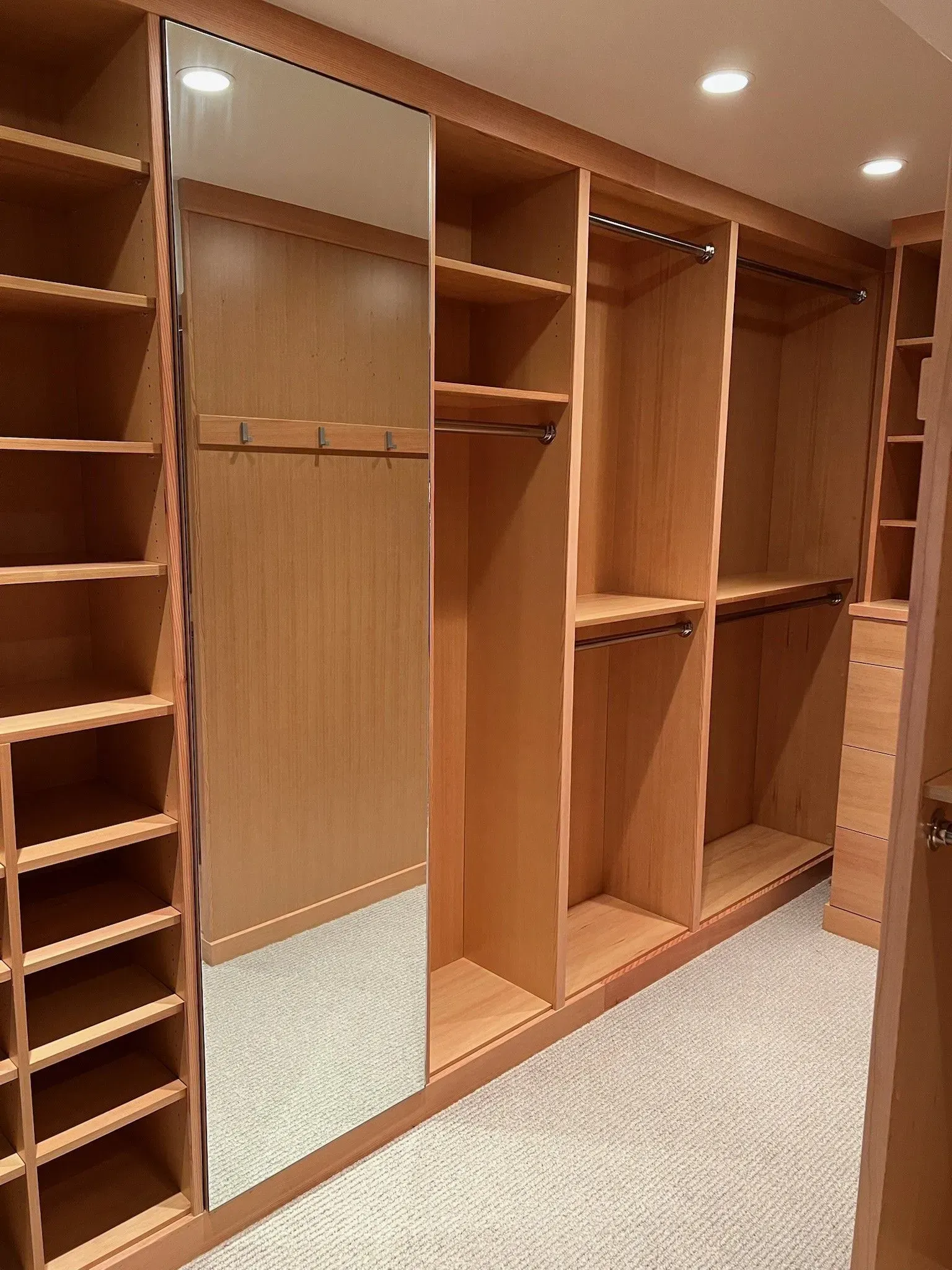 Custom light-wood walk-in closet with open shelving, hanging rods, and a full-length mirror.