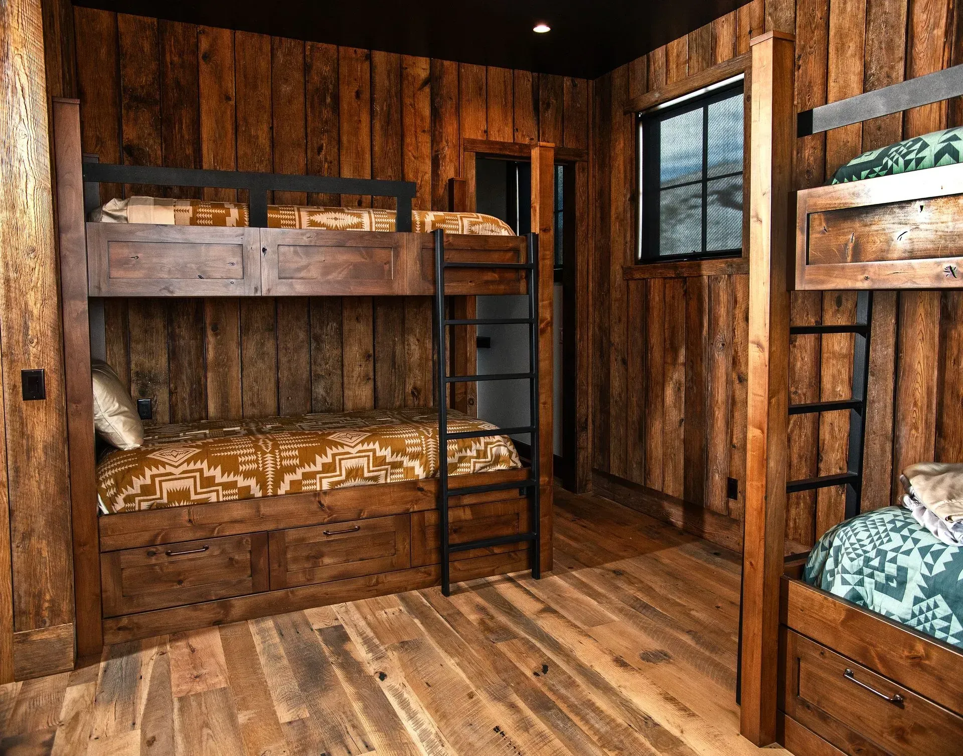 Rustic bedroom with wooden bunk beds, dark walls, and patterned bedding.