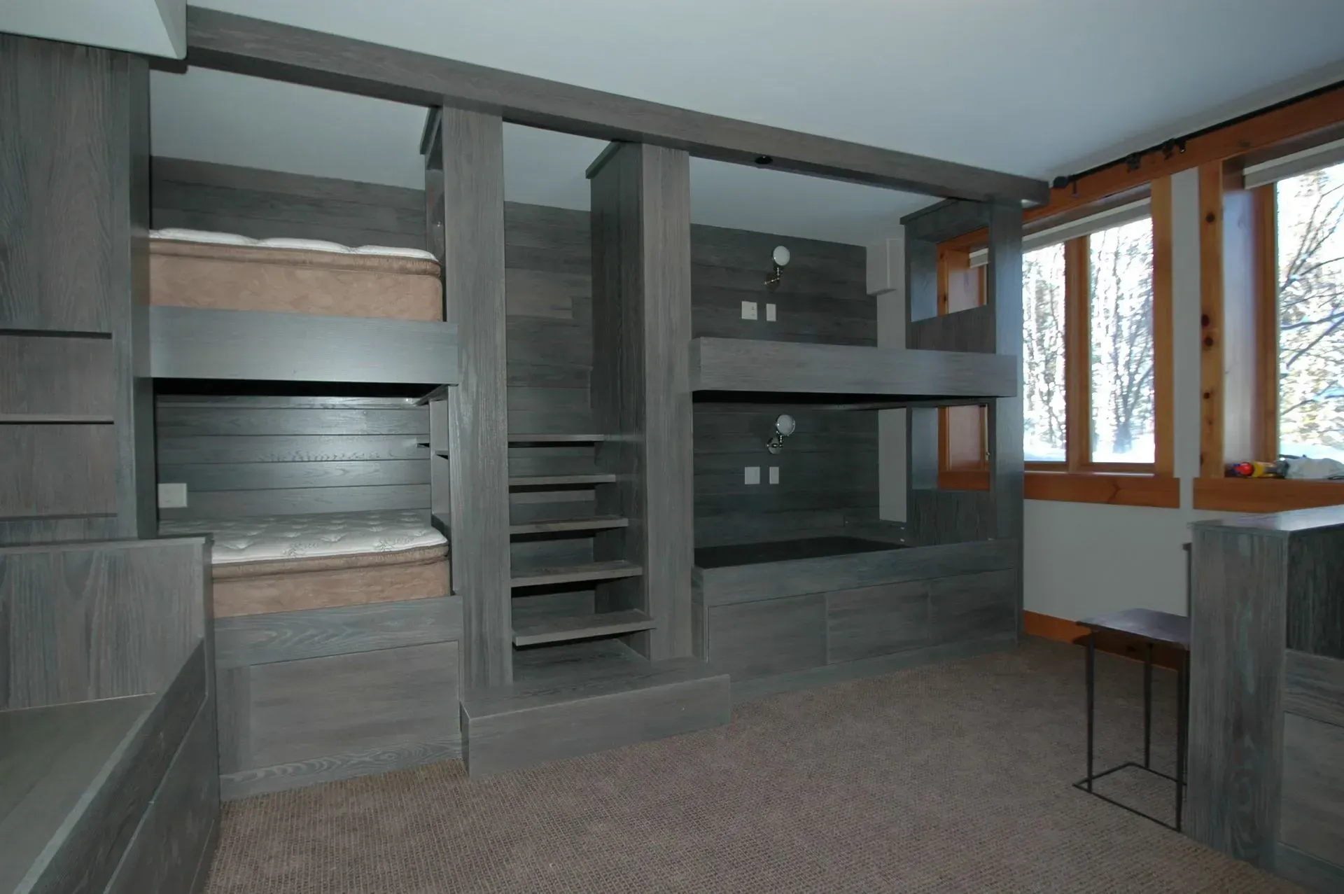 A bedroom featuring built-in wooden bunk beds with integrated stairs, neutral carpet, and windows with outdoor views.
