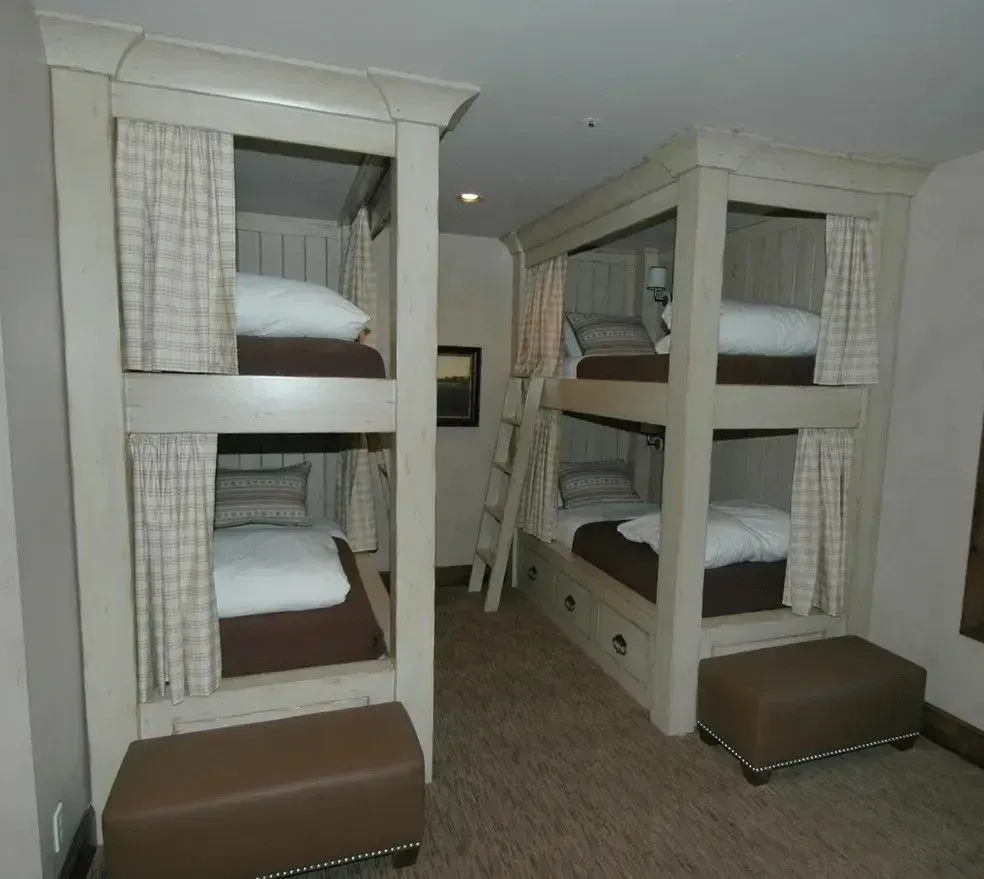 A bedroom featuring two sets of light-wood, built-in bunk beds with beige curtains, white bedding, and brown benches.