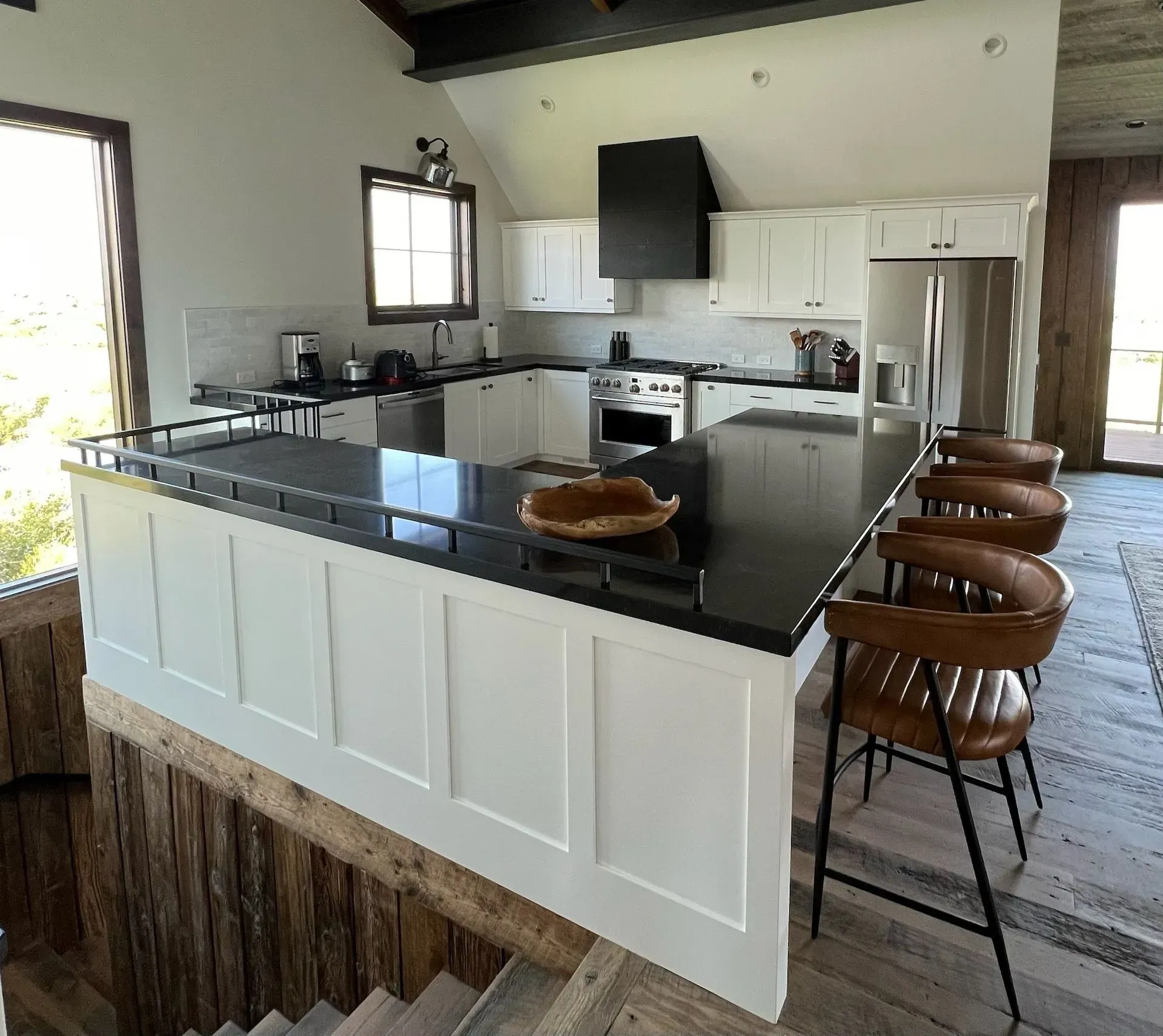 Modern kitchen with a black island, white cabinets, stainless steel appliances, and brown leather bar stools on wood floor.