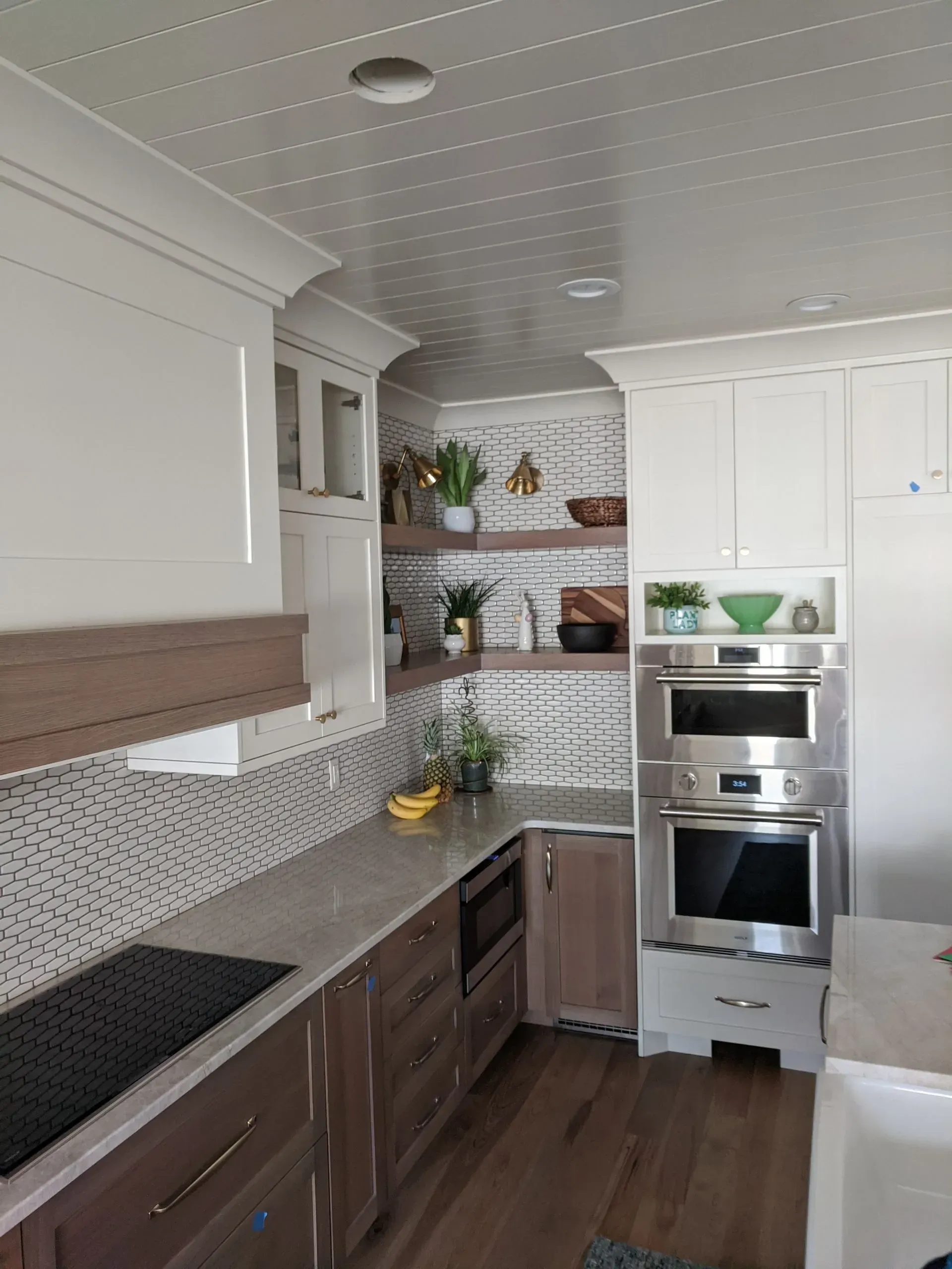 A kitchen with white cabinets, dark wood lower cabinets, a patterned backsplash, and stainless steel wall ovens.