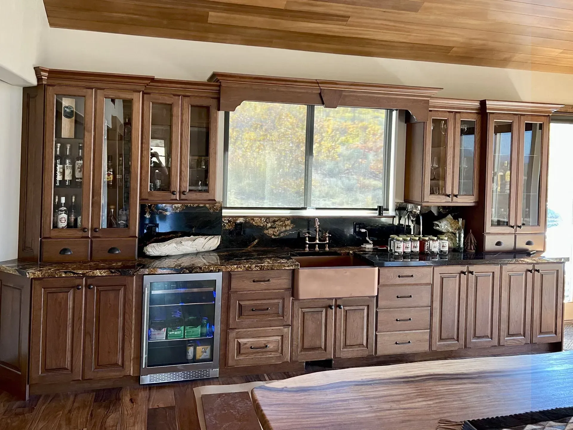A home wet bar with dark wood cabinets, a wine fridge, copper apron sink, and decorative glass-front upper cabinets.
