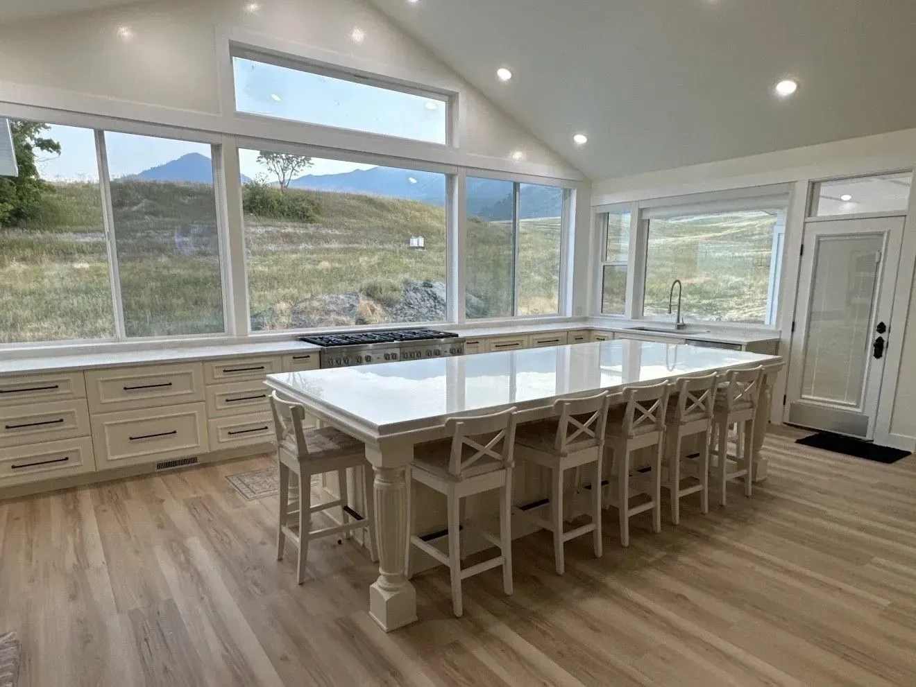 Bright, modern kitchen with white cabinetry, a large marble-topped island with stools, and expansive mountain views.