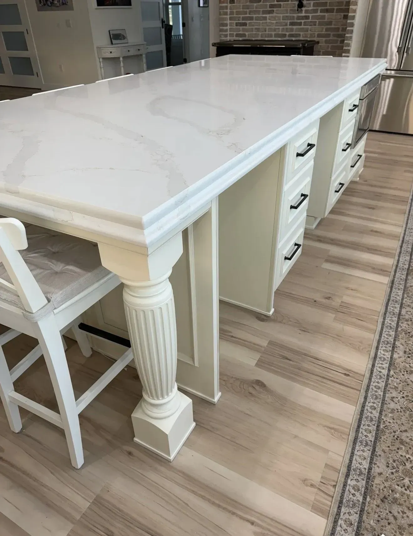 A kitchen island with a white marble-patterned countertop, fluted white support leg, and cream-colored drawers.