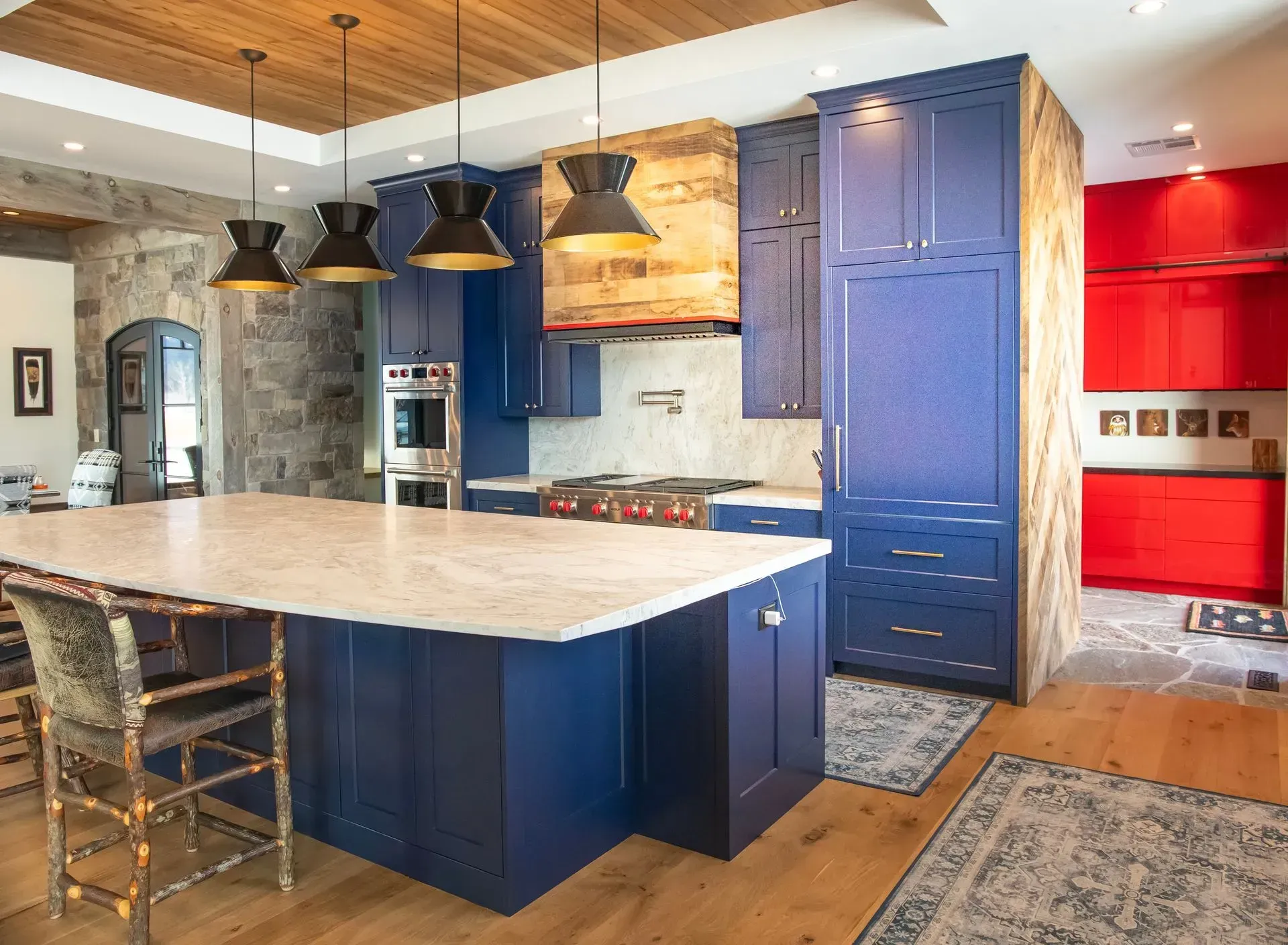 Modern kitchen with a large blue island, light countertop, wooden ceiling, and a vibrant red pantry area.