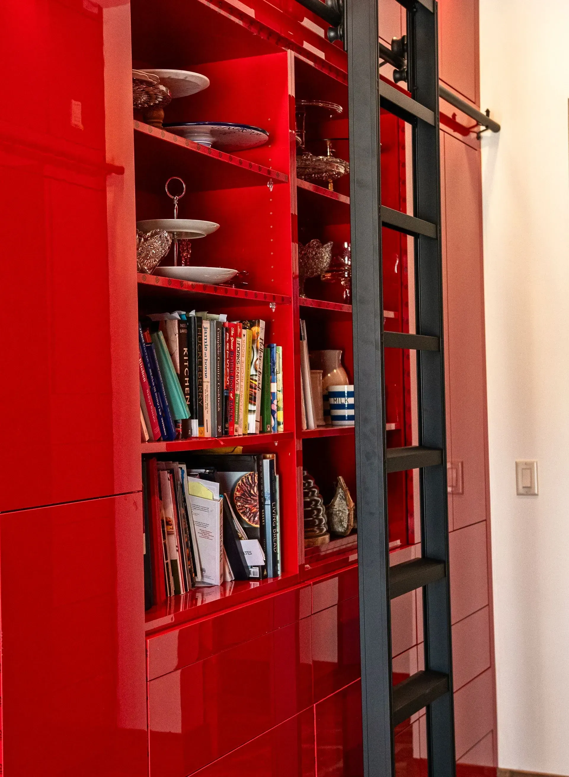 A vibrant red, floor-to-ceiling bookshelf with a black rolling library ladder attached to a top rail.