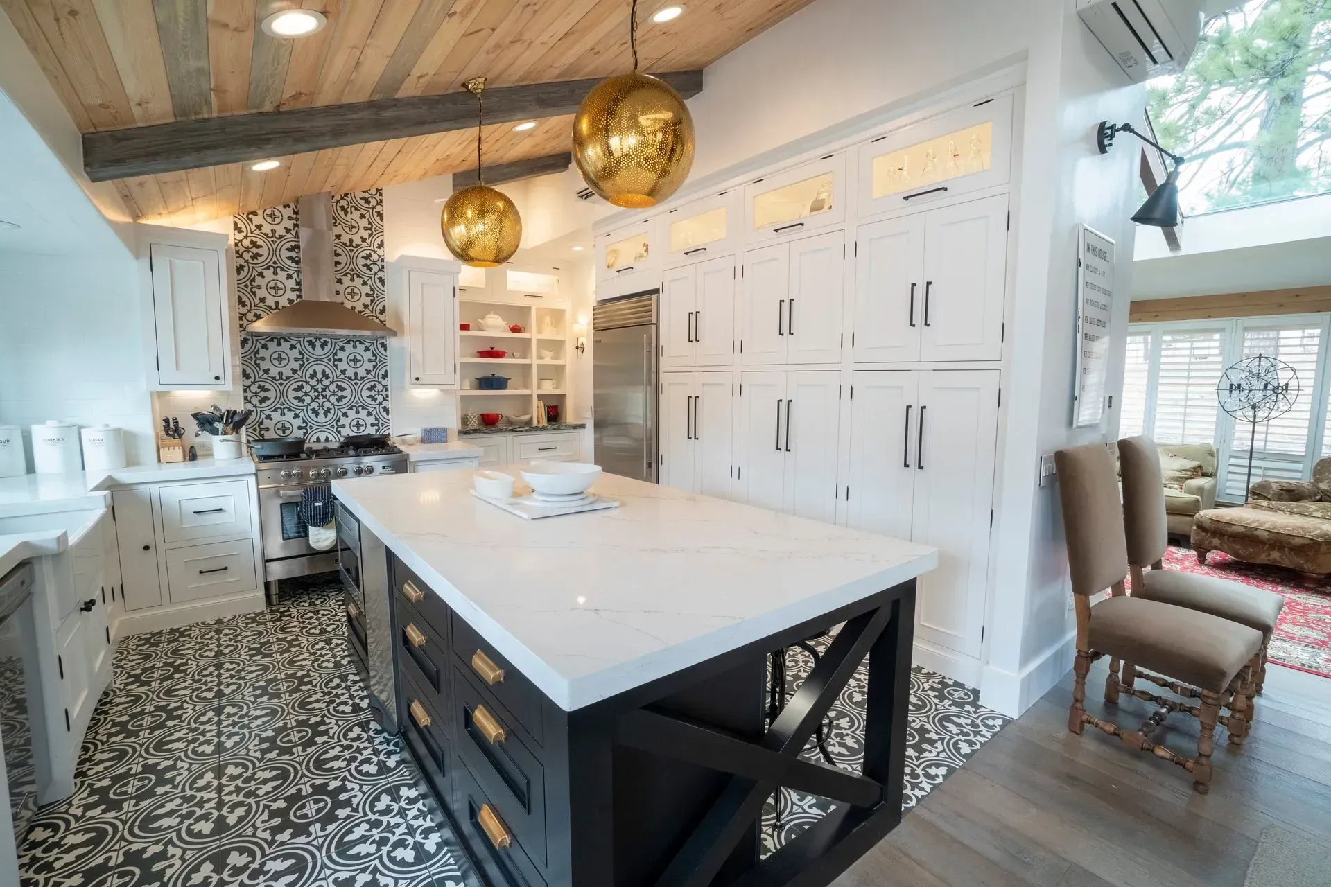 A modern kitchen with a dark central island, white cabinetry, patterned tile floor, and a wood-planked ceiling.