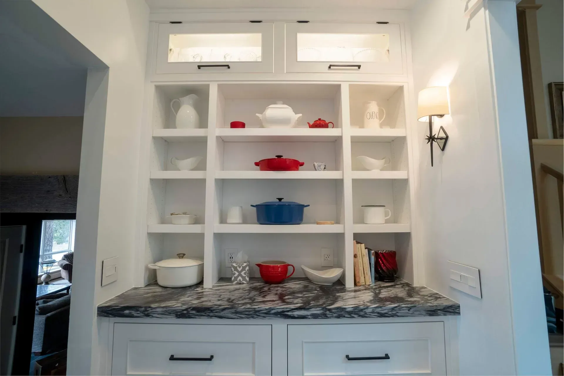 Built-in white hutch with open shelving, displaying colorful pottery and cookware above a dark granite countertop.