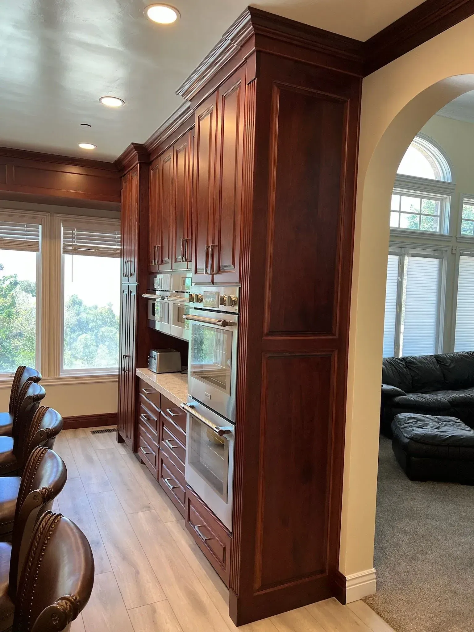 A tall, dark cherry wood kitchen cabinet unit with a built-in double oven, situated next to an arched entryway.