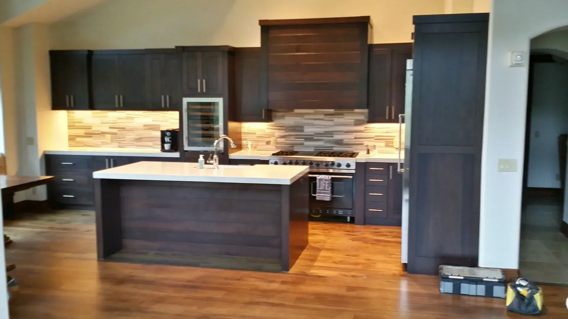 Modern kitchen with dark wood cabinetry, a central island with white countertops, and wood flooring.