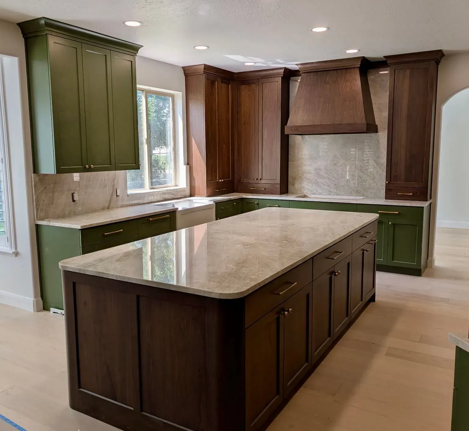 A kitchen featuring a large central island with dark wood cabinets and a light stone countertop, paired with green cabinets.