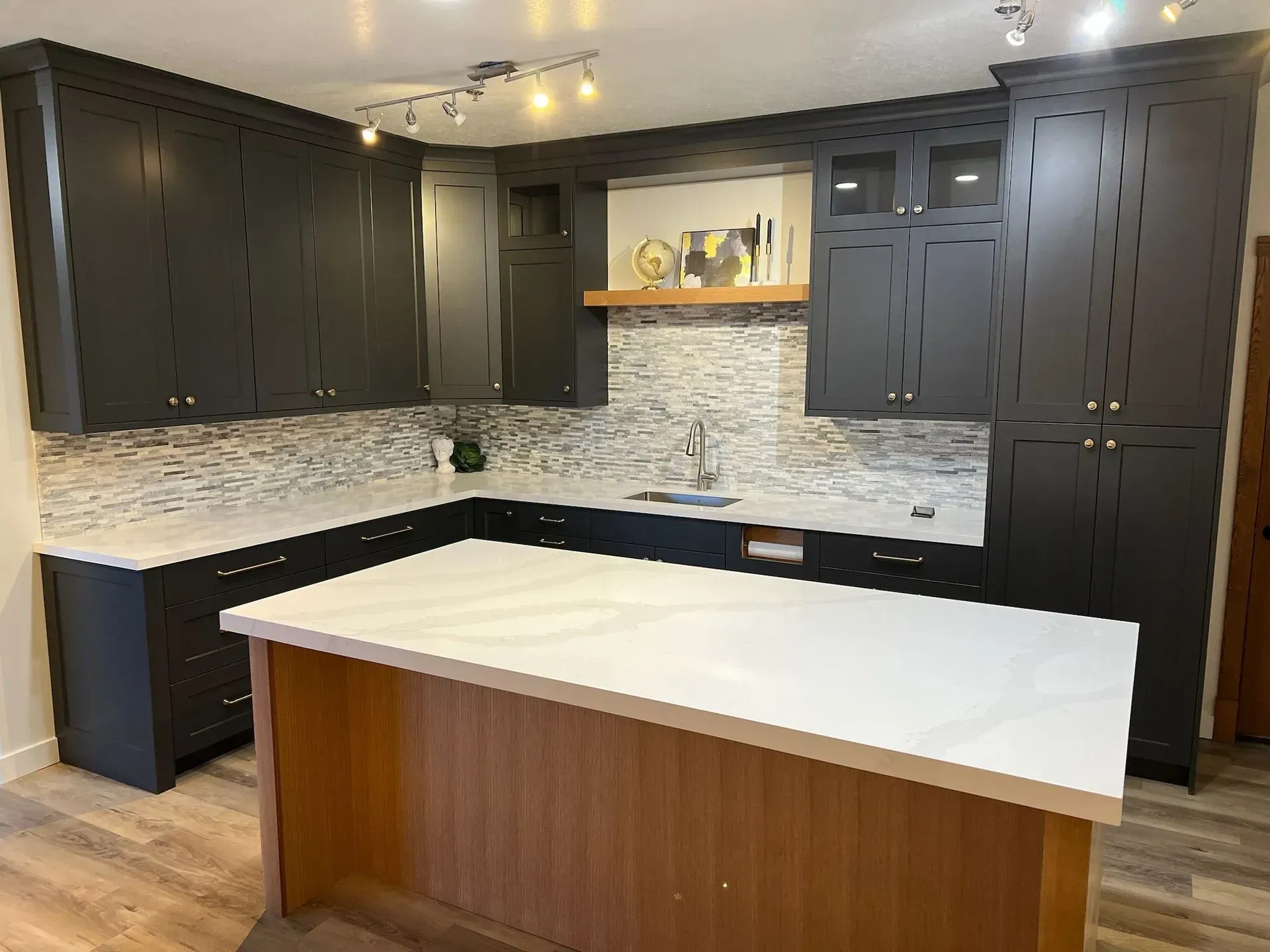 A modern kitchen featuring black cabinetry, a white stone-topped island, a wood base, and a light-toned stone backsplash.