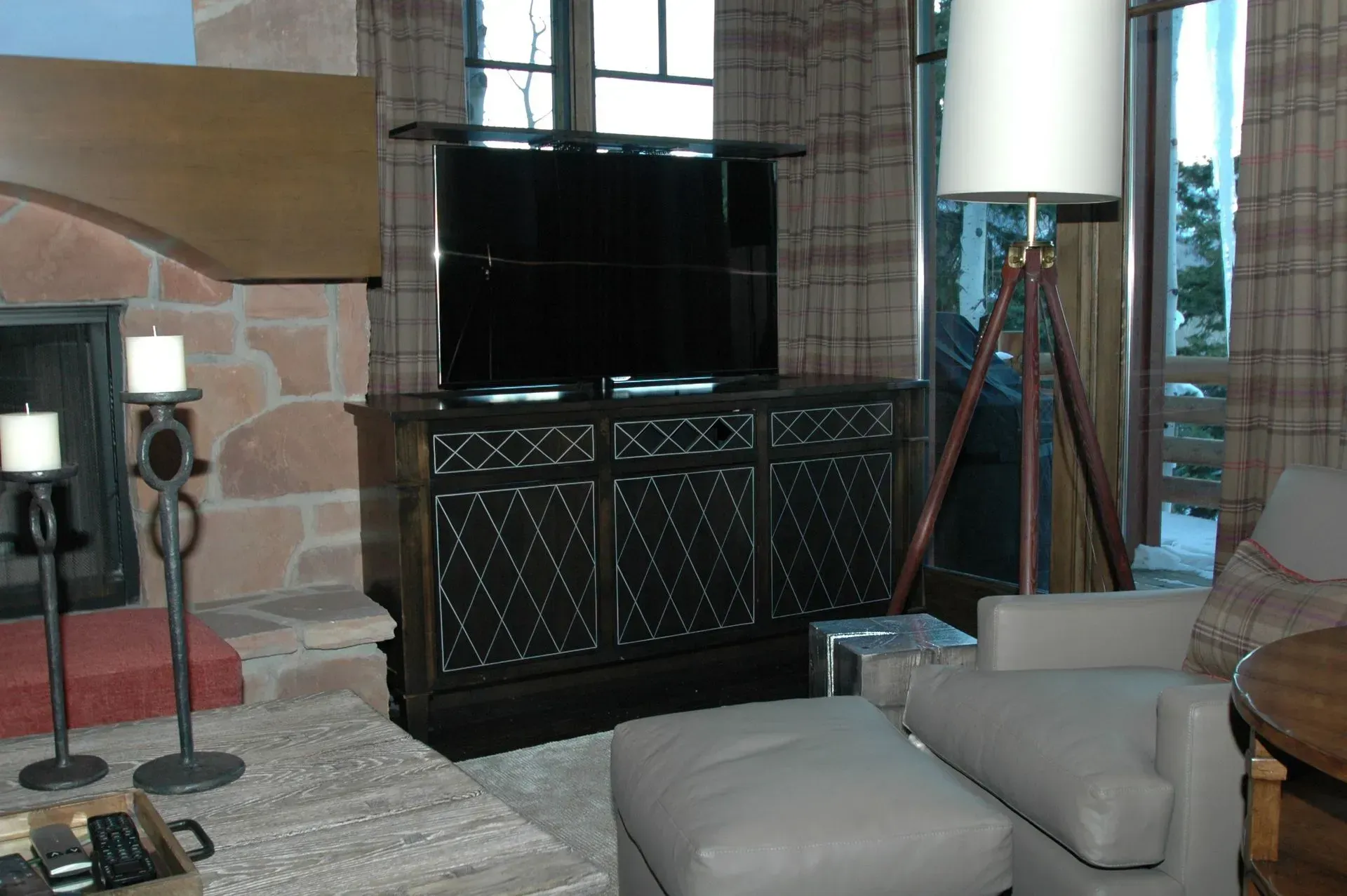 A living room with a stone fireplace, a dark patterned cabinet topped by a television, and a tripod floor lamp.