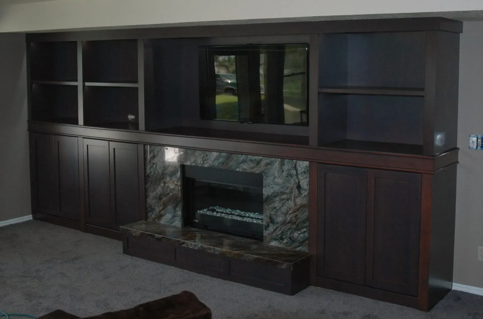 Dark wood built-in shelving unit surrounding a fireplace with a stone mantel and a wall-mounted flat-screen television.