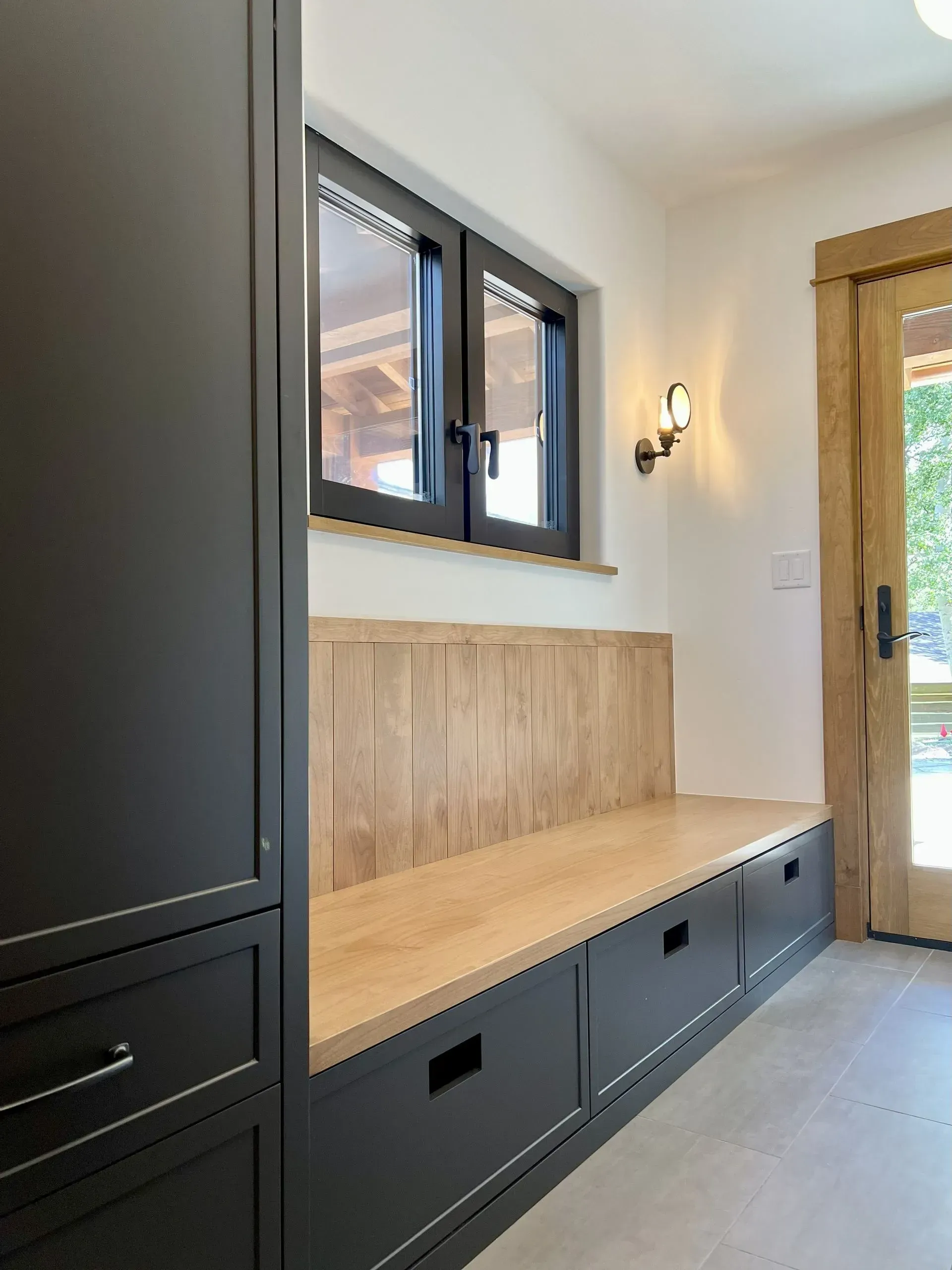 Built-in entryway bench with black cabinets and drawers, topped with a light wood seat and matching wood wall paneling.