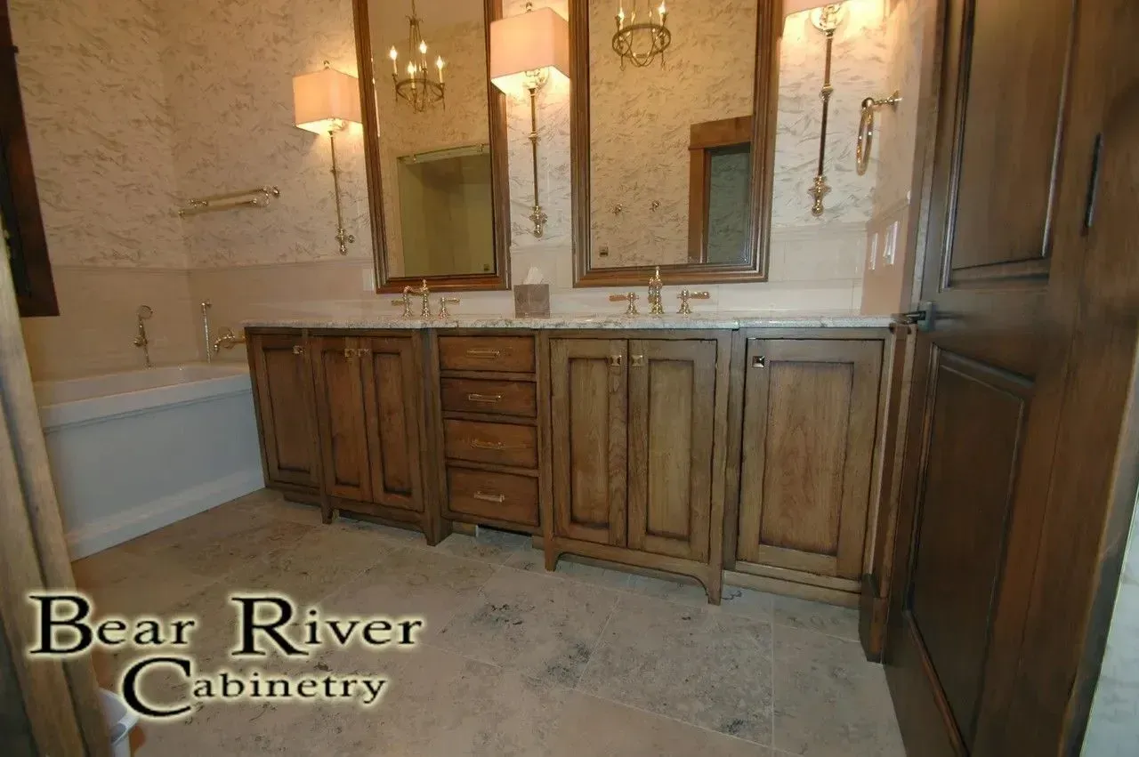 Double wood vanity with marble countertop and two mirrors in a bathroom with patterned wallpaper and a bathtub.
