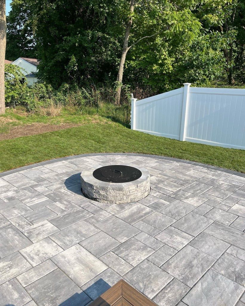 A fire pit on a patio with a white fence in the background.