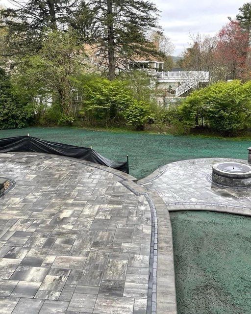 A patio with a fire pit and a pool in the background.