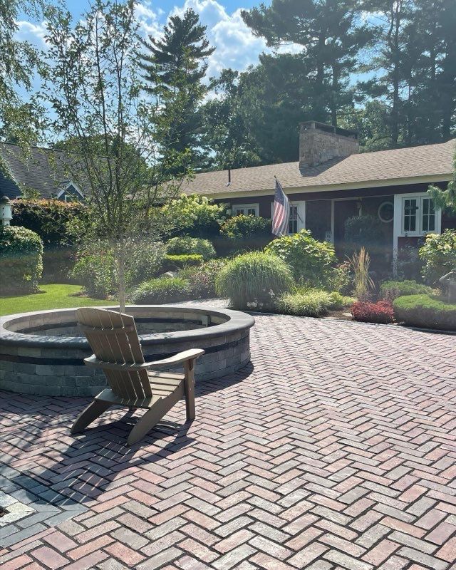 A wooden chair sits on a brick patio next to a fire pit.