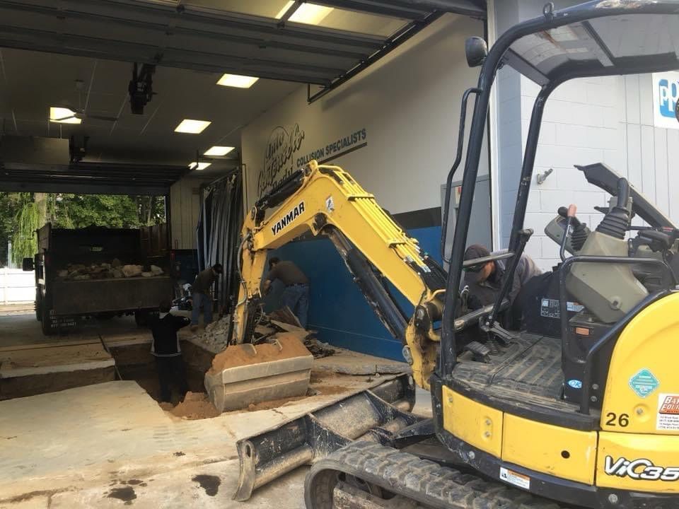 A yellow excavator is sitting in a garage next to a truck.