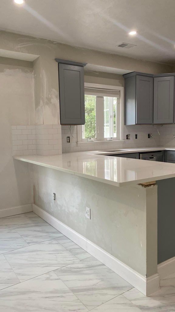 A kitchen with gray cabinets and white counter tops is being remodeled.