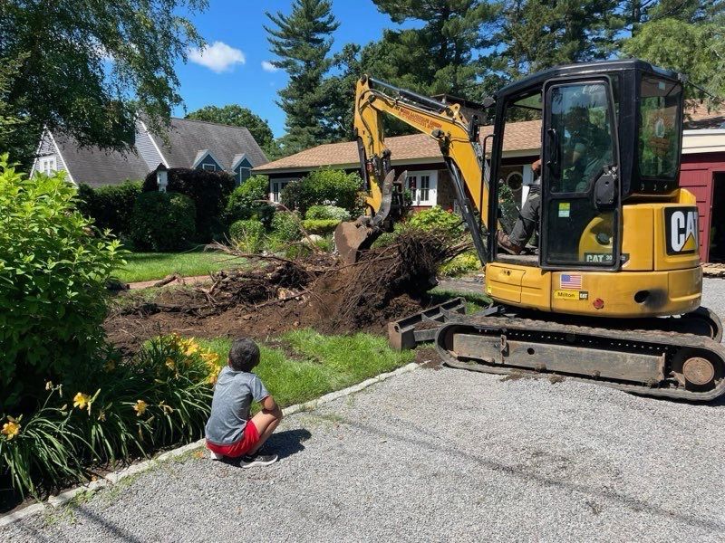 A boy is sitting in front of a cat excavator.