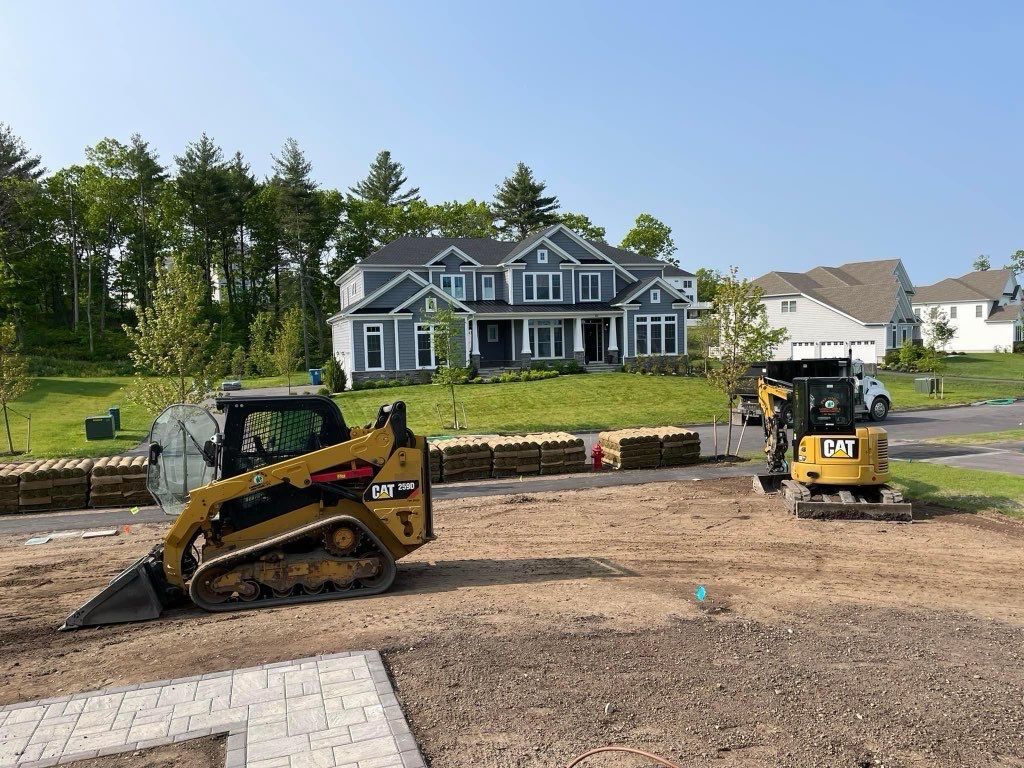 Two bulldozers are working on a dirt field in front of a house.
