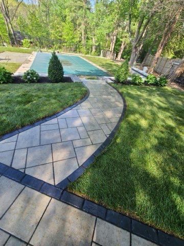 A brick walkway leading to a swimming pool in a backyard.