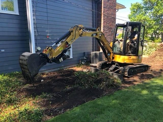 A small yellow excavator is sitting in front of a house.
