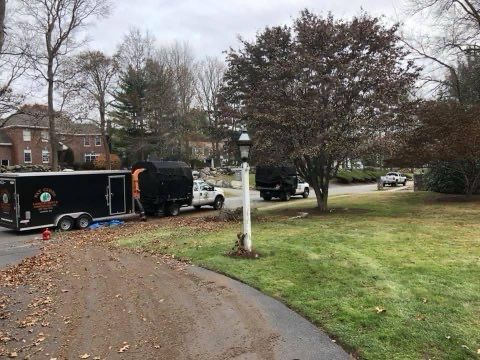 A black trailer is parked in a driveway next to a white truck.