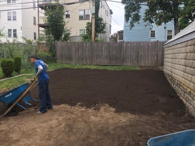 A man is using a wheelbarrow to move dirt in a backyard.