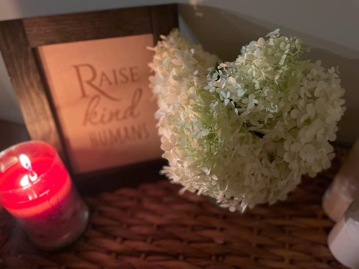 A picture frame that says raise kind humans next to a heart shaped flower and a candle