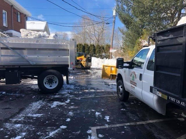 A white truck is parked in a parking lot next to a dump truck.