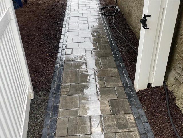 A brick walkway with a white fence in the background