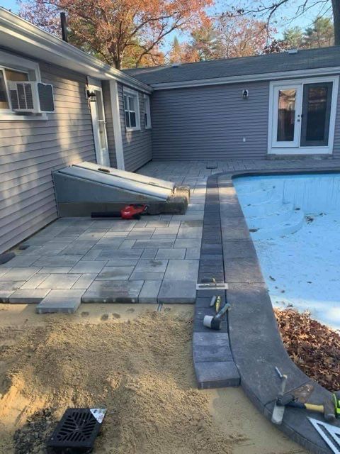 A patio is being built next to a pool in front of a house.