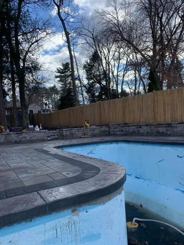 An empty swimming pool with a wooden fence in the background.