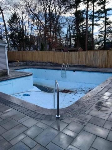 An empty swimming pool with a wooden fence in the background.