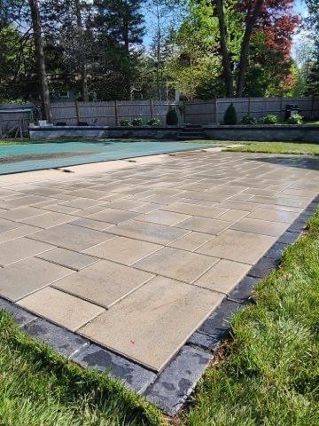 A large patio next to a swimming pool in a backyard.