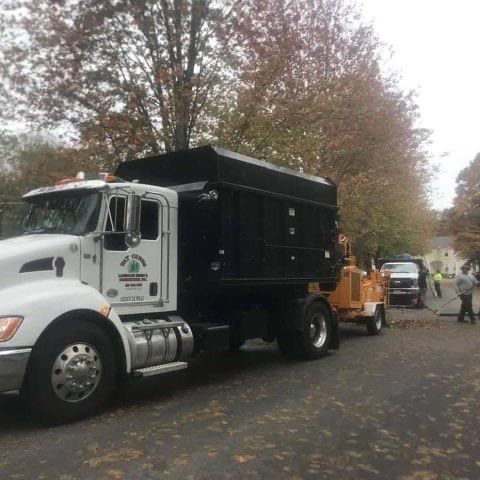 A dump truck is parked on the side of the road next to a tree chipper.