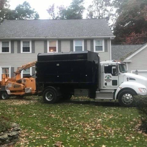 A truck with a tree chipper attached to it is parked in front of a house.