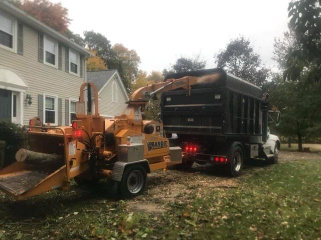 A tree chipper is parked next to a dump truck in front of a house.
