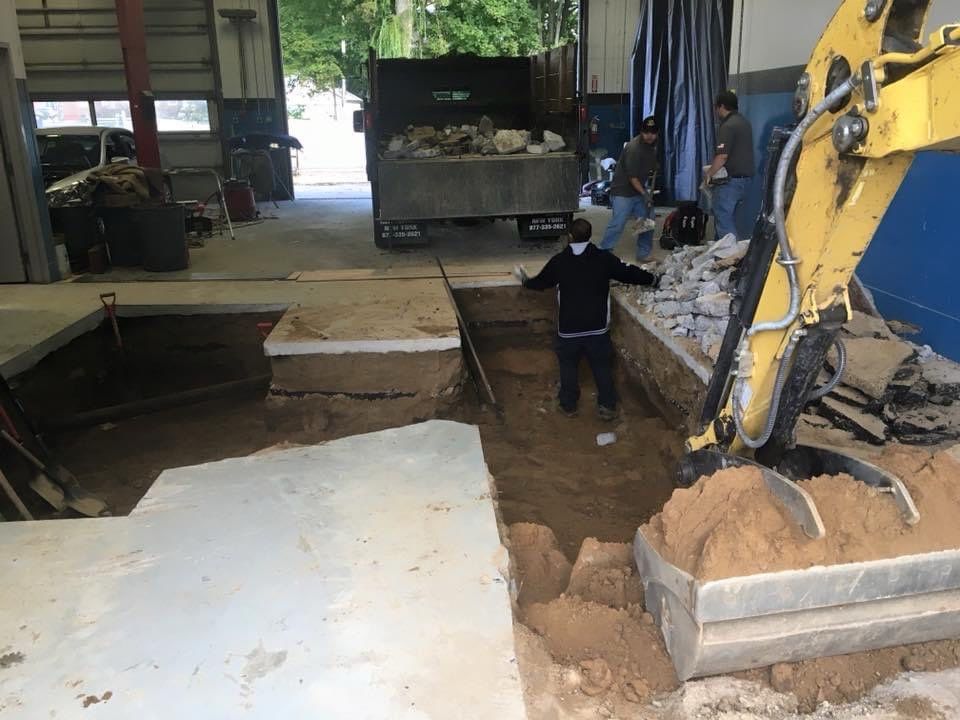 A man is standing in the dirt next to a yellow excavator.