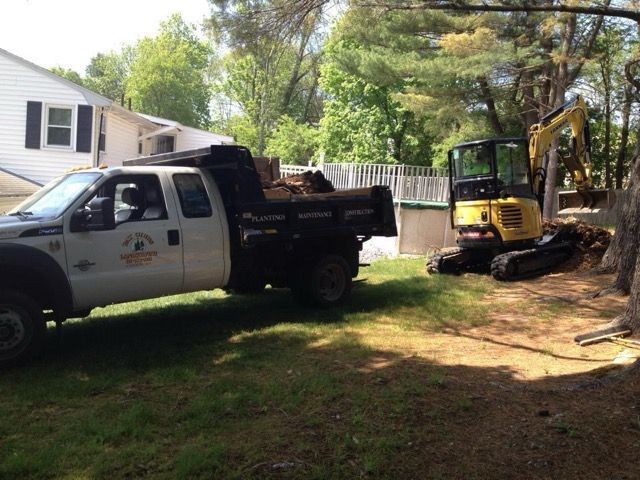 A dump truck is parked in front of a house next to an excavator.