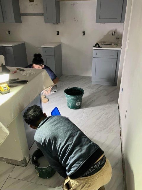A man is kneeling down in a kitchen under a sink.